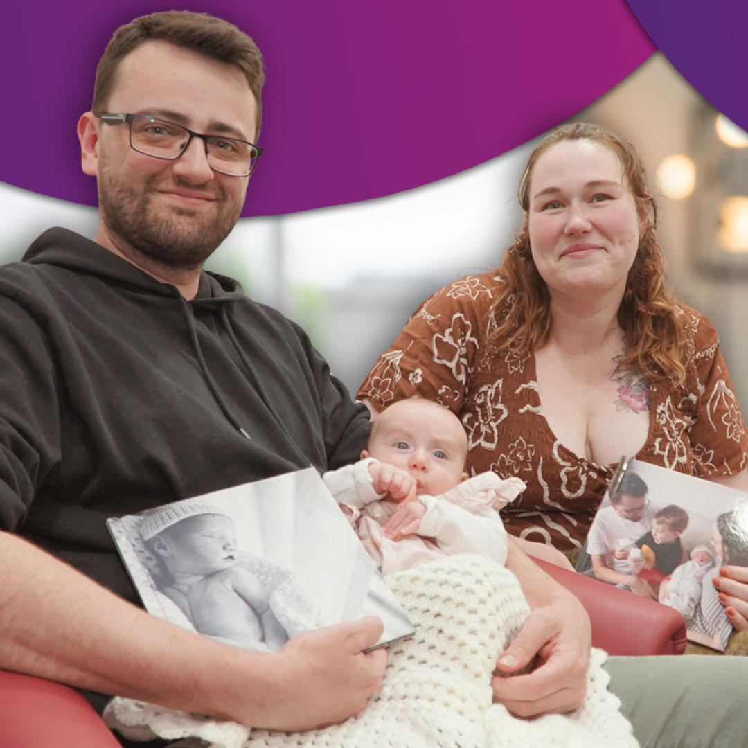 Morgan and Dylan sitting together, holding baby Violet and photo books of their daughter Eloise, who was born still. They smile gently at the camera, reflecting love, remembrance, and connection during Pregnancy and Infant Loss Remembrance Month.
