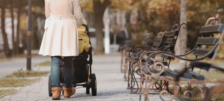 Woman walking while pushing a pram through a park in autumn. 