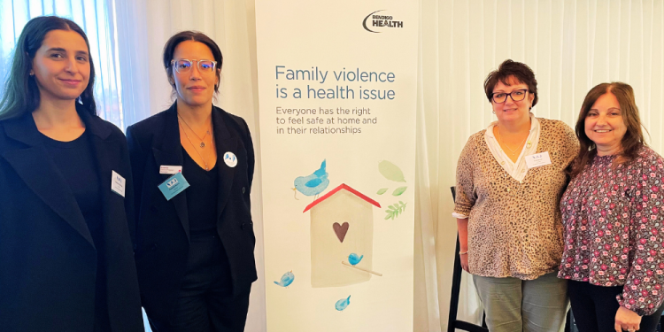 Two women stand on the left hand side of a pull up banner with information about family violence with another two women standing to the righ