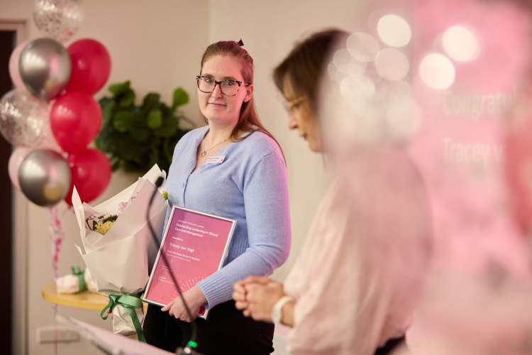 Midwife Tracey poses with a certificate, flowers and balloons.