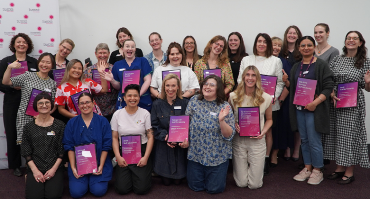 A large group of scholarship recipients, standing and kneeling, holding their framed certificates, some laughing and waving. 